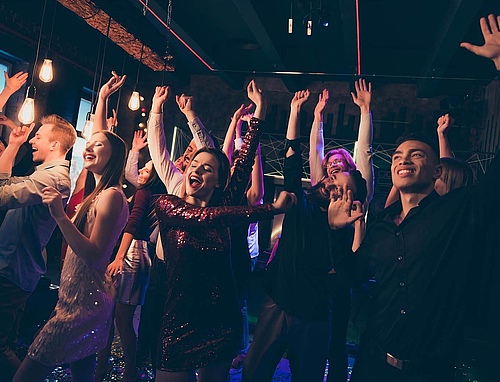 Begeisterte Jugendliche tanzen im Club und heben jubelnd die Arme in die Luft – pulsierende Energie und Lebensfreude auf der Tanzfläche.