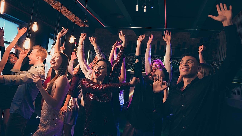 Begeisterte Jugendliche tanzen im Club und heben jubelnd die Arme in die Luft – pulsierende Energie und Lebensfreude auf der Tanzfläche.